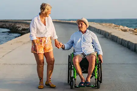 man in wheelchair holding wife's hand on pier